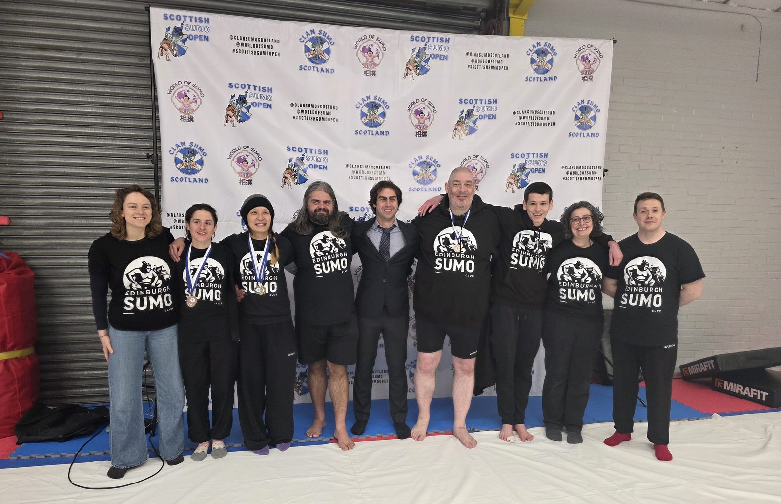 The Edinburgh Sumo Club squad with medals in front of the Scottish Sumo Open backdrop.